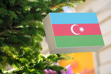 Azerbaijan flag printed on a Christmas gift box. Printed present box decorations on a Xmas tree branch on a street.