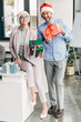 © LIGHTFIELD STUDIOS - happy businessman and businesswoman in santa hats holding gift boxes and smiling at camera in office