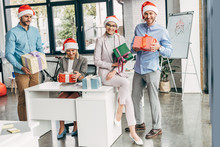 Happy Young Start Up Team In Santa Hats Holding Christmas Presents At Workplace