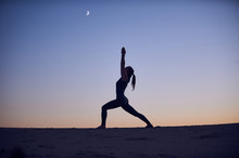Beautiful Young Woman Practices Yoga Asana Virabhadrasana 1 - Warrior Pose 1 In The Desert At Night