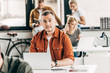 © LIGHTFIELD STUDIOS - handsome young man working with laptop at open space office and looking at camera with colleagues on background