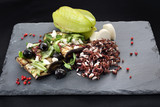 Fototapeta  - Sałatka z grillowanym bakłażanem. Grillowany bakłażan z czarnymi oliwkami, serem feta i zielonymi warzywami podany z dzikim ryżem na czarnym kamiennym talerzu.