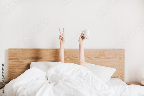 Cuadros en Lienzo Hand's of young woman with coffee mug in bed with white linens