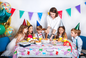 Family celebrating kids birthday. Parents and children celebrate together. Child party with balloon decoration, cake, candles and presents.