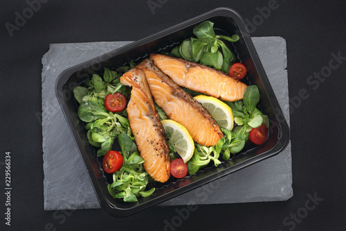 Fototapeta na szkło Kawałki pieczonego łososia na sałacie. Gotowe danie na wynos zapakowane w lunch box.