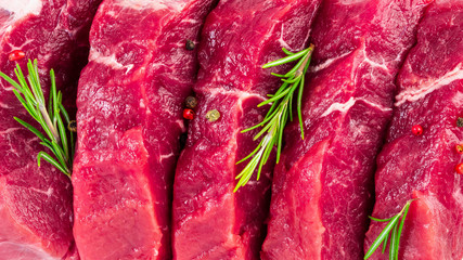 Wall Mural - background of fresh raw sliced beef steaks, garlic, rosemary and seasonings. Juicy meat banner, top view, macro close up