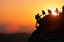 Silhouette Of The Climbing Team Helping Each Other While Climbing Up In A Sunset. The Concept Of Aid.