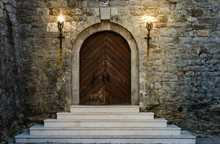 Old Wooden Doors Of Ancient Castle With White Staircase Are Illuminated By Burning Torches.