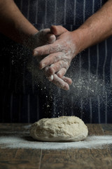 Flour is sprinkled over a ball of dough on wooden board by hand