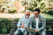 © bnenin - Two elegant men sitting in the park looking at laptop screen.
