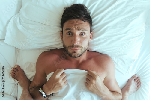 Fotografie, Obraz handsome man laying naked in bedroom is surprised over his girlfriend standing upon him dominating