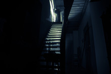 Inside Of Old Creepy Abandoned Mansion. Staircase And Colonnade. Silhouette Of Horror Ghost Standing On Castle Stairs To The Basement. Spooky Dungeon Stone Stairs In Old Castle With Light.