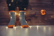 Kids Legs In Stylish Colorful Striped Socks In Garland Lights On Floor With Pumpkins In Room. Decor For Halloween, Cosy Moment. Cozy Autumn Days. Happy Halloween Celebration Concept. Vintage Tone 