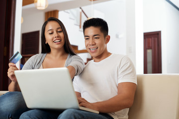 Joyful young mixed-race couple with credit card shopping online