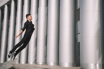 young male dancer in black clothes jumping on street