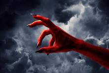 Halloween Red Devil Monster Hand With Black Fingernails Against A Dark Sky