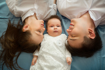 beautiful young family mom and dad lie on the bed with the little daughter at home