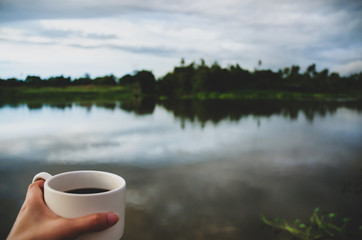 Wall Mural - White coffee cup in hand At the waterfront in the morning.Morning coffee.Do not focus on objects.