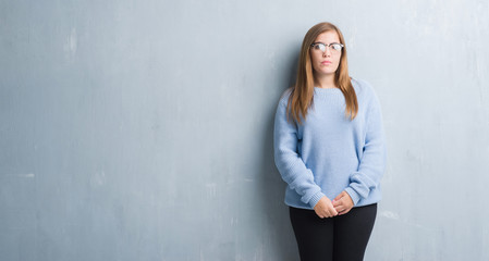 Poster - Young adult woman over grey grunge wall wearing glasses with serious expression on face. Simple and natural looking at the camera.