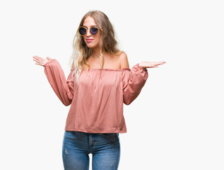 Poster - Beautiful young blonde woman wearing retro sunglasses over isolated background clueless and confused expression with arms and hands raised. Doubt concept.