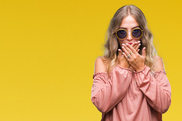 Canvas Print - Beautiful young blonde woman wearing retro sunglasses over isolated background shocked covering mouth with hands for mistake. Secret concept.