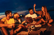 © Zoran Zeremski - Group of young friends enjoying at the lake at night. They sitting around the fire singing and having fun at camping.