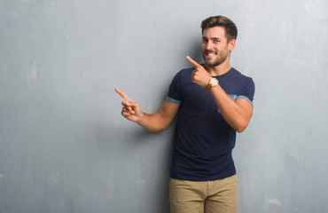 Poster - Handsome young man over grey grunge wall smiling and looking at the camera pointing with two hands and fingers to the side.