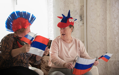 Two happy elderly women watching TV in russian accessories