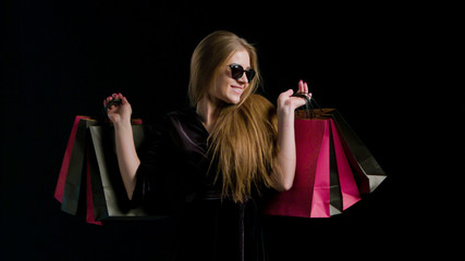 Wall Mural - Woman in cool sunglasses and black dress, holding black shopping bag isolated on dark background in black friday holiday or christmas