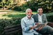 © bnenin - Two business men sitting in the park and using tablet.