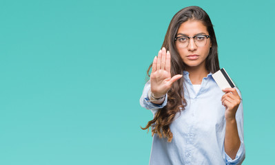 Wall Mural - Young arab woman holding credit card over isolated background with open hand doing stop sign with serious and confident expression, defense gesture