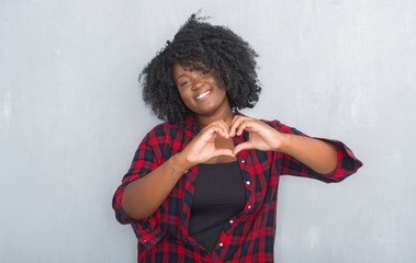 Poster - Young african american hipster woman over grey grunge wall smiling in love showing heart symbol and shape with hands. Romantic concept.