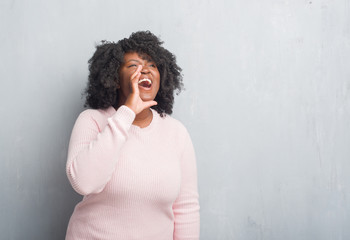 Canvas Print - Young african american plus size woman over grey grunge wall wearing winter sweater shouting and screaming loud to side with hand on mouth. Communication concept.