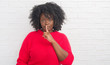 © Krakenimages.com - Young african american plus size woman over white brick wall asking to be quiet with finger on lips. Silence and secret concept.