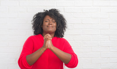 Poster - Young african american plus size woman over white brick wall begging and praying with hands together with hope expression on face very emotional and worried. Asking for forgiveness. Religion concept.