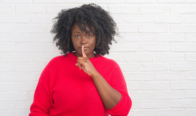 Poster - Young african american plus size woman over white brick wall asking to be quiet with finger on lips. Silence and secret concept.