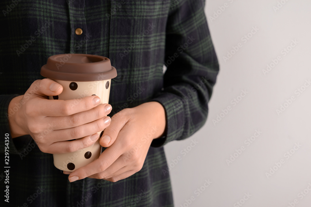 Woman holding coffee cup on light background, closeup