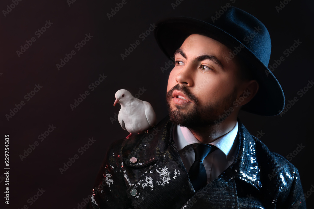Male magician with white pigeon on dark background