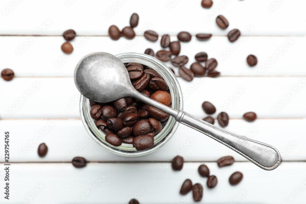 Glass jar with coffee beans on white wooden table
