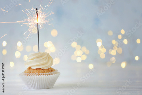 Delicious cupcake with sparkler on white table against blurred lights Wallpaper Mural