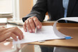 © DragonImages - Close-up of businessman examining business contract and signing it at the office desk