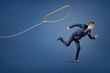 © gearstd - A businessman in a suit runs away from a rope lasso that tries to catch him.
