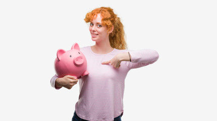 Sticker - Young redhead woman holding piggy bank with surprise face pointing finger to himself