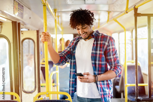 Fotografie, Obraz Young modern Afro-American man standing in a public transport and listening to the music