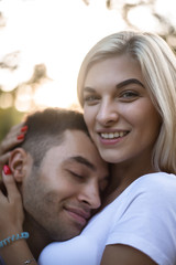 Wall Mural - Loving couple standing on grass in nature green park with beautiful sundown light hugging. Man lies on woman's breast.