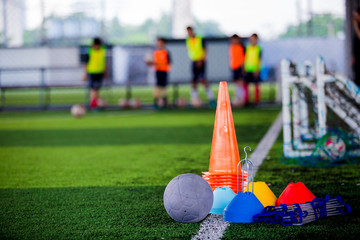 Football and soccer training equipment on green artificial turf with blurry player training background.