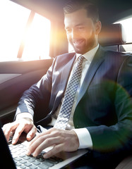 Wall Mural - businessman sitting in the back-seat of a car, using his laptop