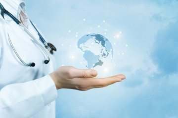 a female doctor with a stethoscope on her neck is holding a crystal, sparkling global map on her han