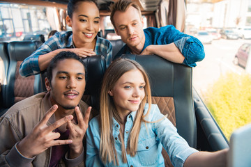 Wall Mural - happy multiethnic friends taking selfie on smartphone during trip on travel bus