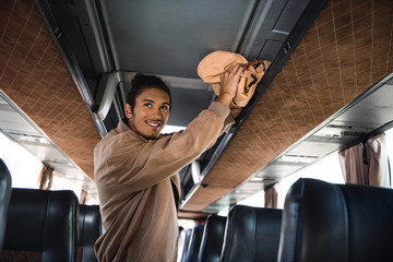 Wall Mural - smiling young multiracial man putting rucksack on shelf in travel bus